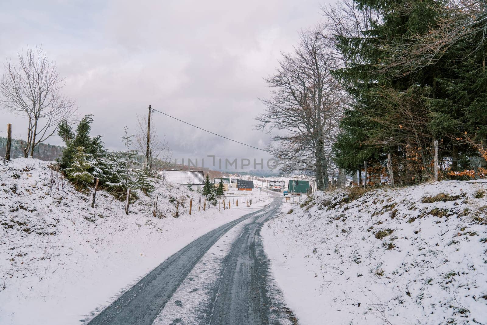 Highway through snowy forest to village with colorful houses in mountain valley. High quality photo