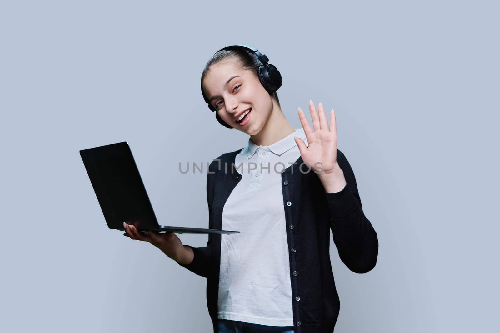 Teen girl student wearing headphones using laptop, on grey background by VH-studio