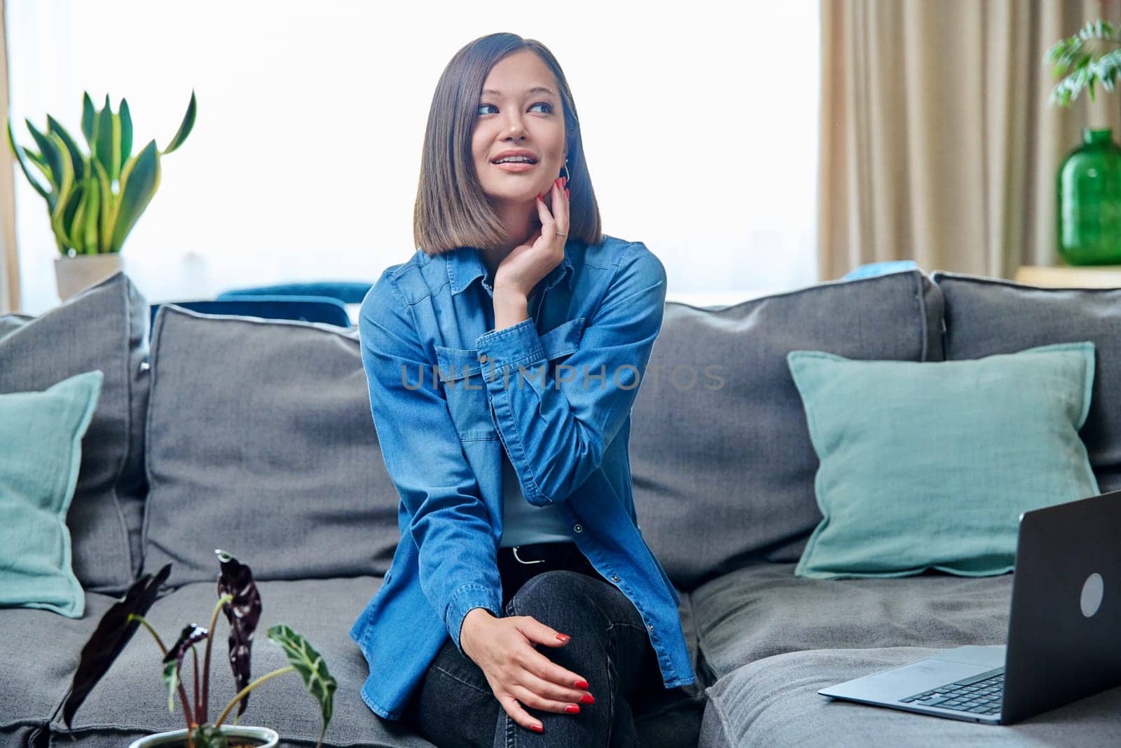 Portrait of young smiling attractive woman looking at camera, sitting on sofa in living room at home. Lifestyle, leisure, youth concept