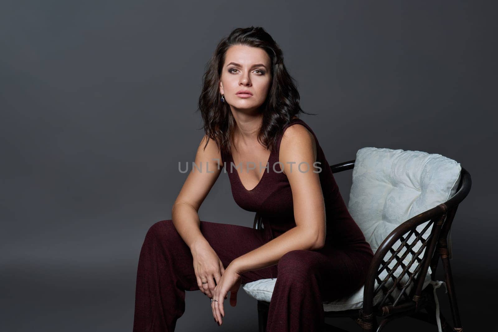 Fashionable sensual attractive young woman posing sitting in chair on dark gray studio background. Beauty, fashion, style concept