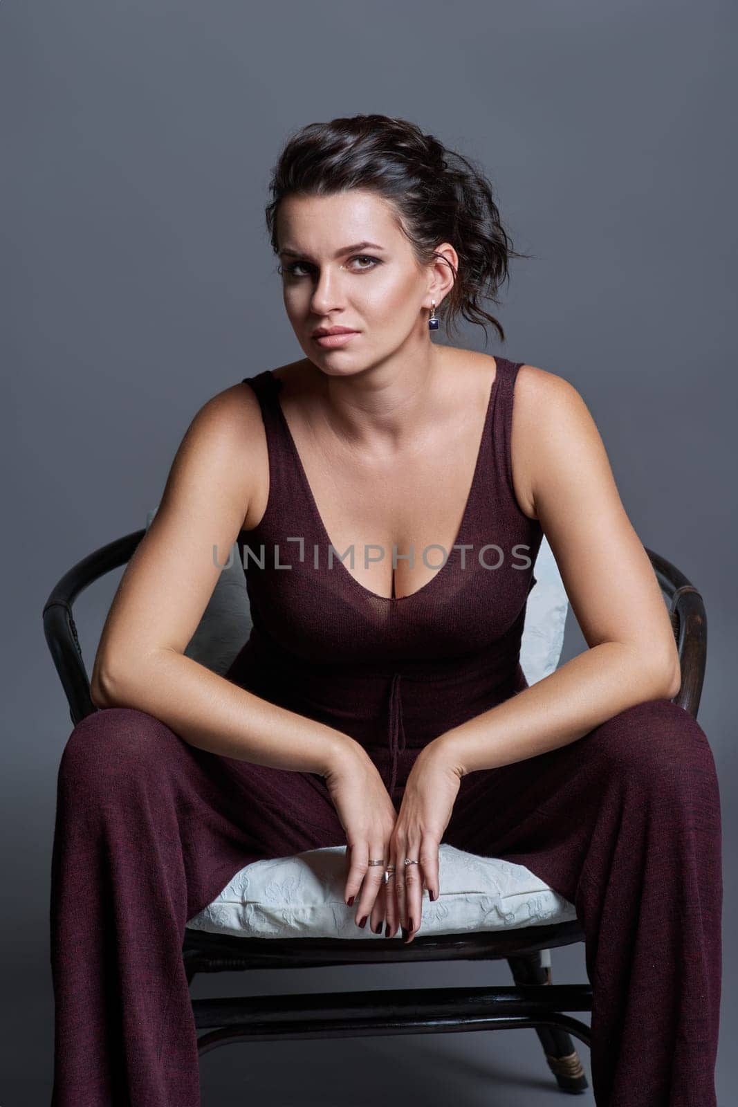 Fashionable sensual attractive young woman posing sitting in chair on dark gray studio background. Beauty, fashion, style concept