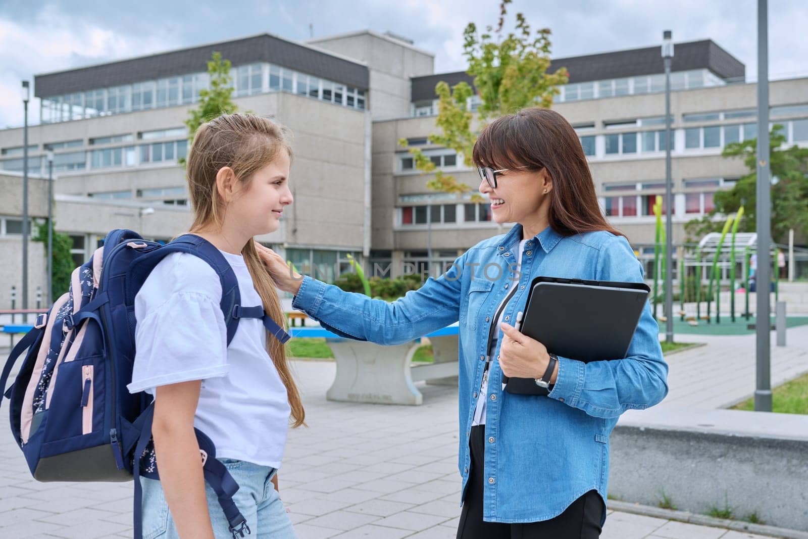 Talking teacher and schoolgirl child outdoor, school building background by VH-studio