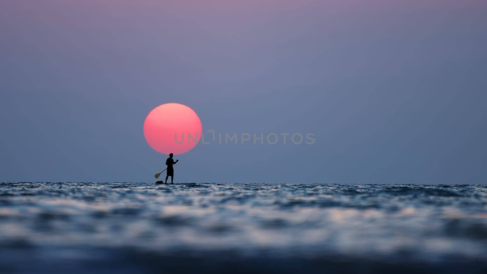 silhouette of a man on the paddleboard against the setting sun. Paddleboard in the sea at sunset, side view . Young man on paddle boarding during a beautiful sunrise. Paddle-boarding by open water.