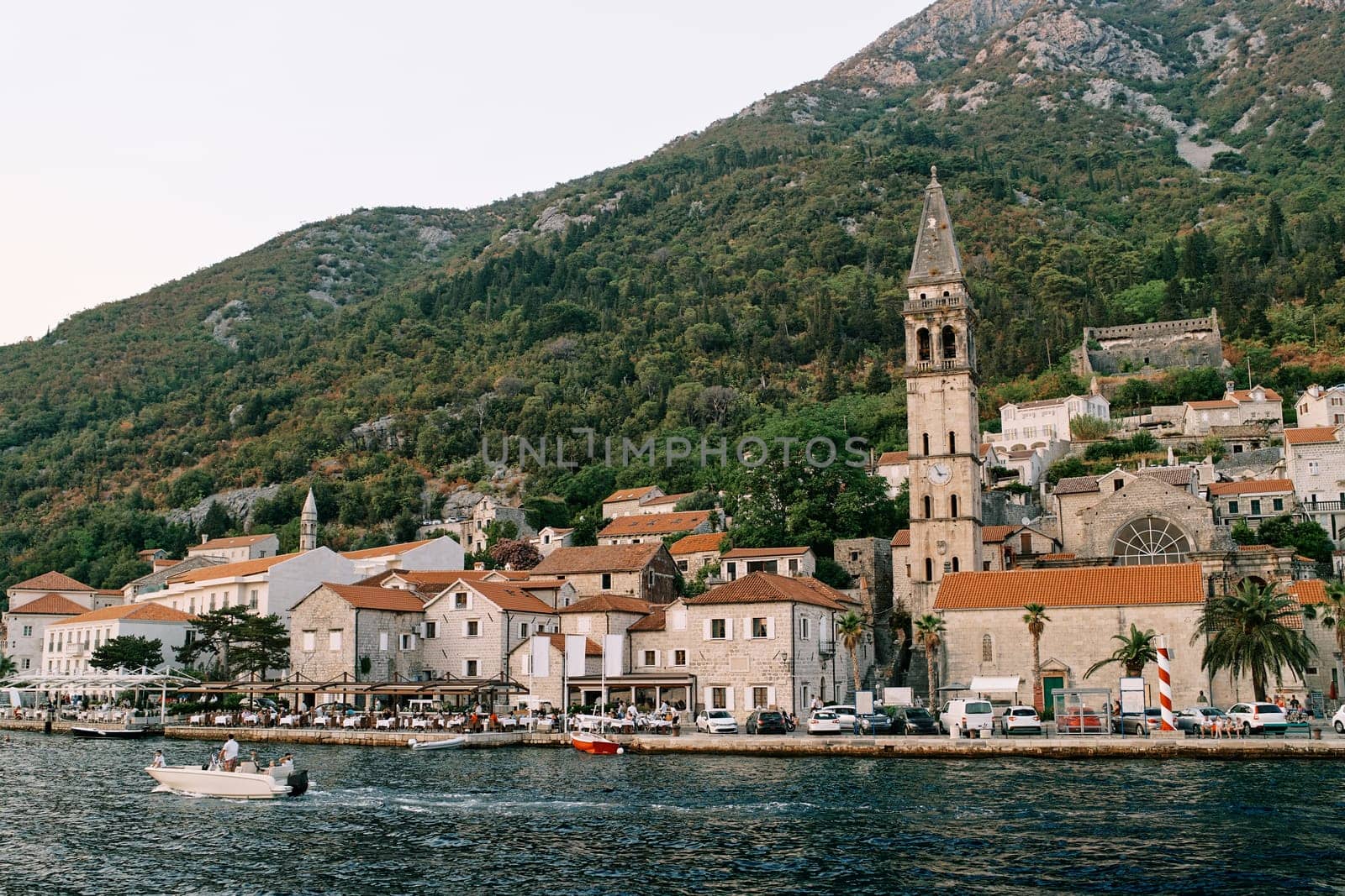 Motor boat sails along the shore with ancient houses and a bell tower. Perast, Montenegro. High quality photo