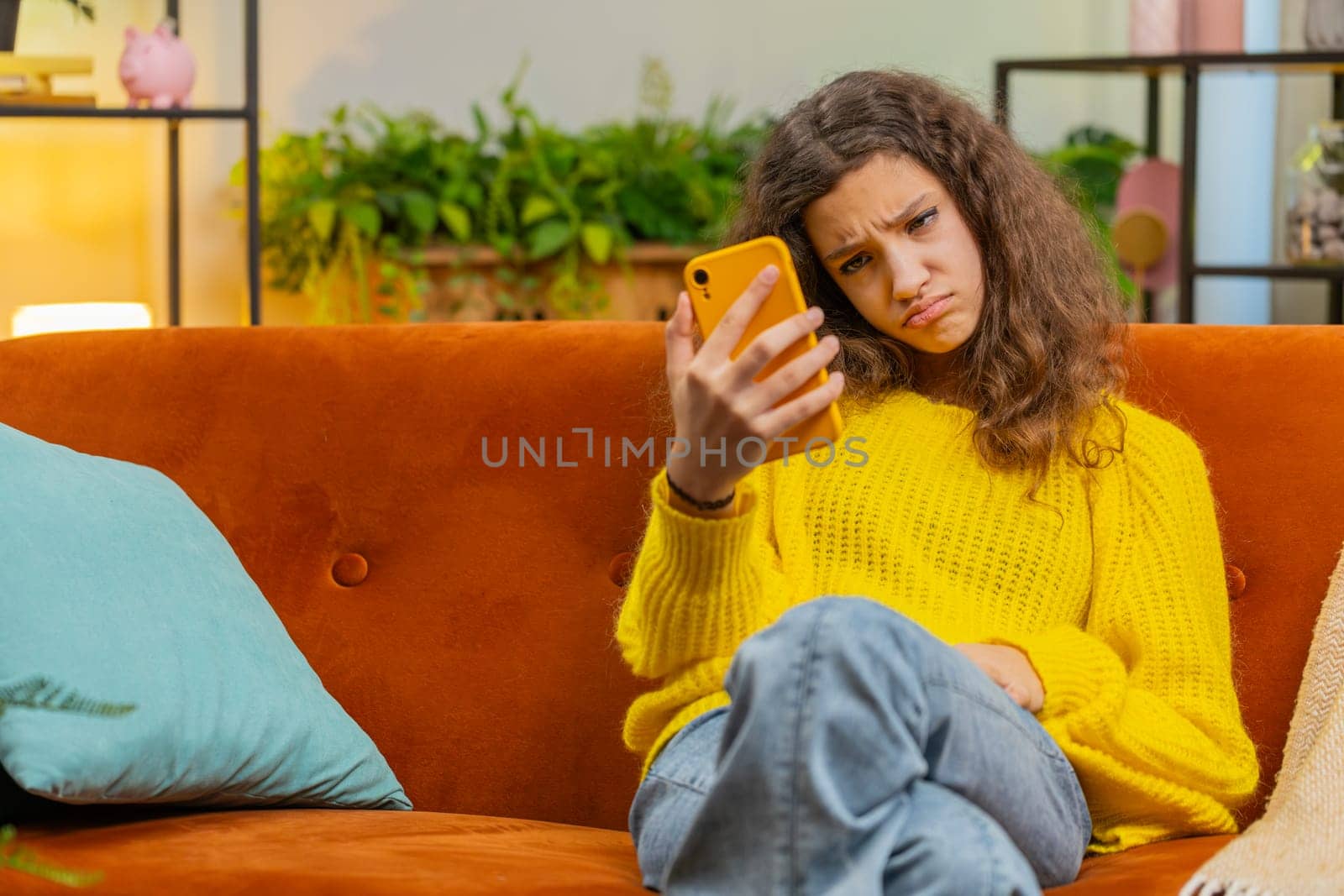 Child girl use smartphone, playing game, loses becoming surprised sudden lottery results, bad news, fortune loss fail education study test. Teenager kid at home in living room sits on sofa. Copy-space