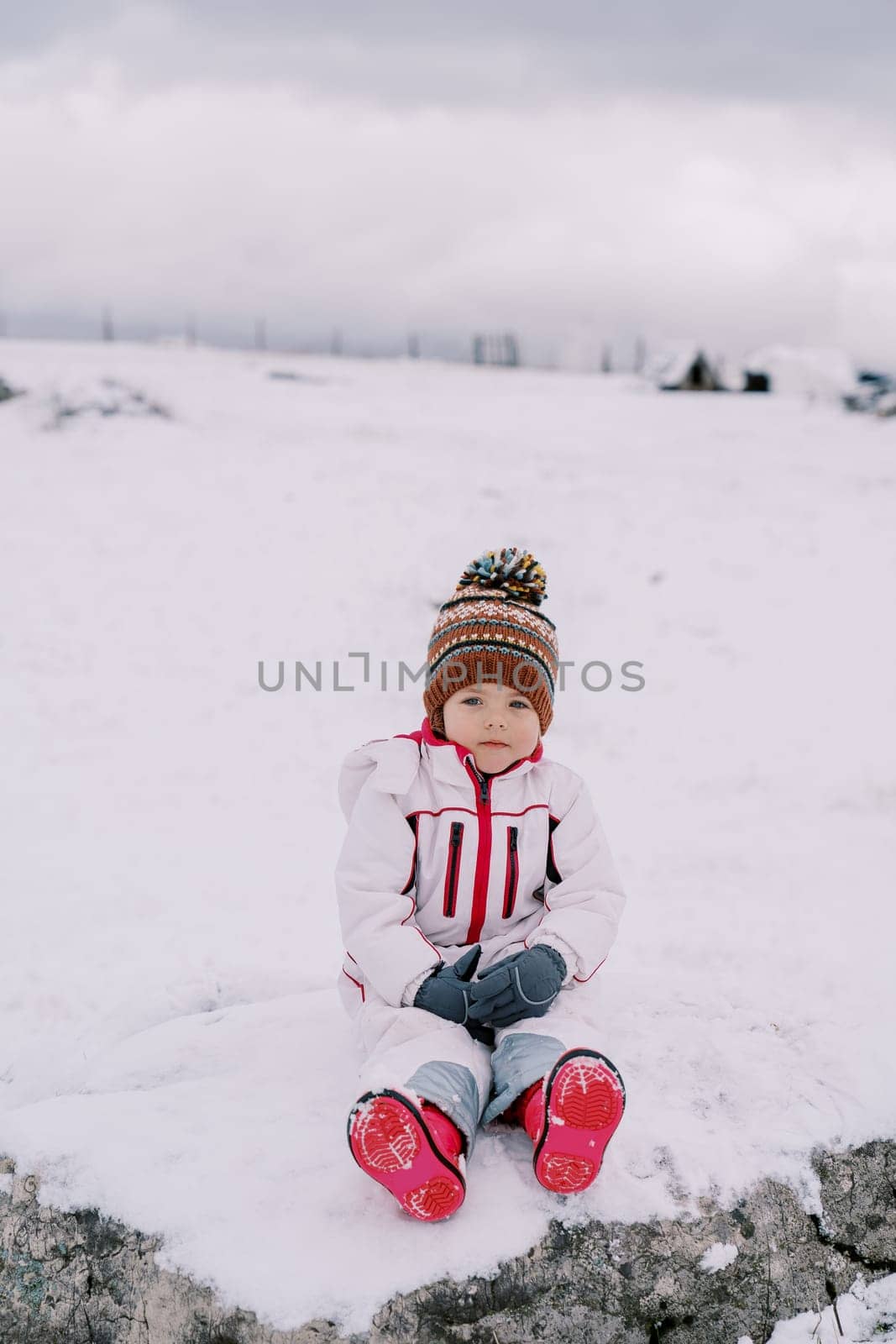 Little girl sitting on a snowy pasture by Nadtochiy