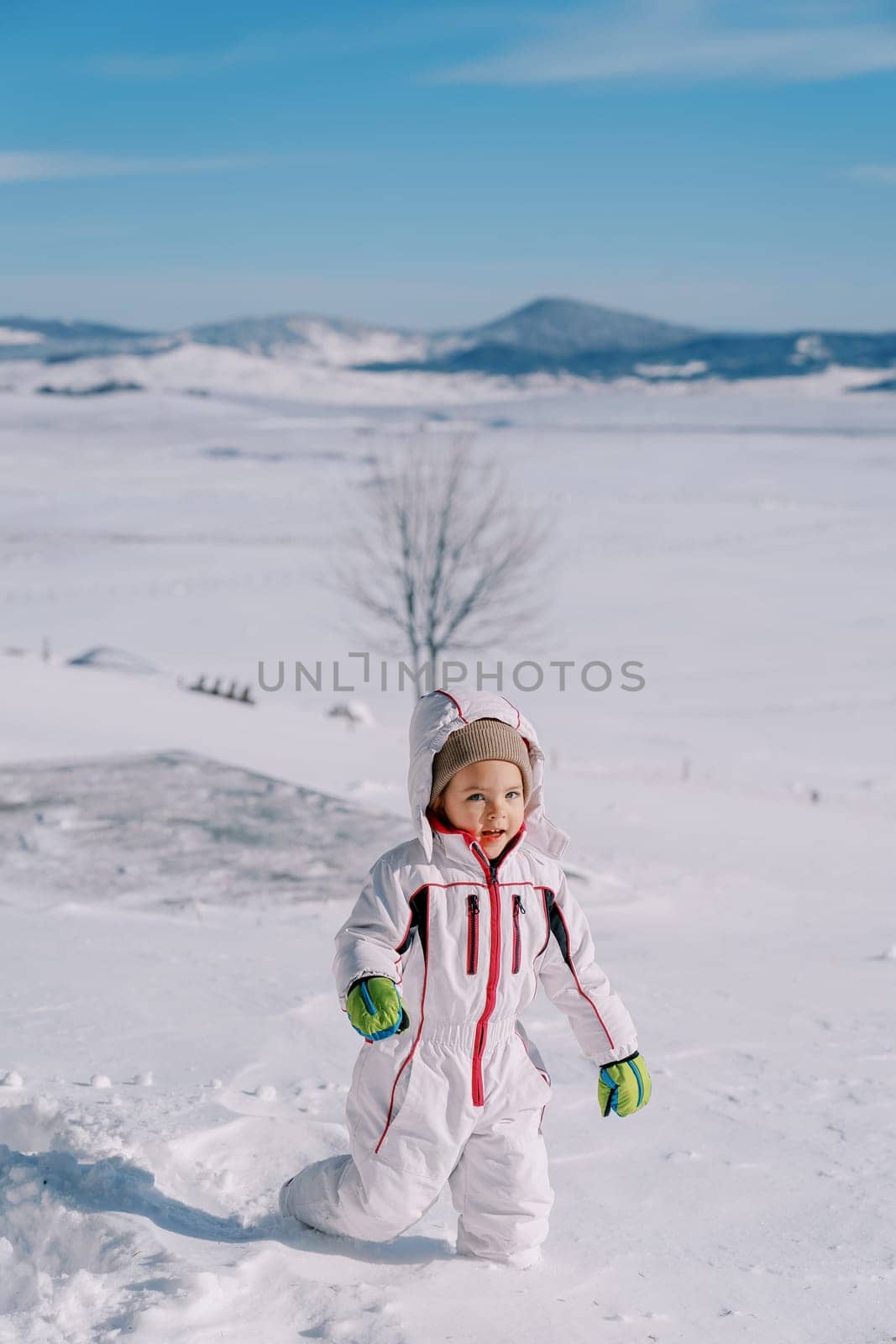 Little smiling girl walks through deep snowdrifts in a mountain valley by Nadtochiy