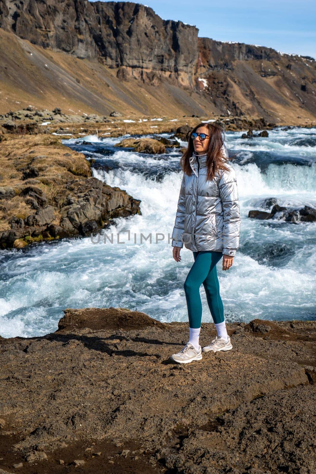 Woman next to a river and waterfall in Iceland on a sunny day