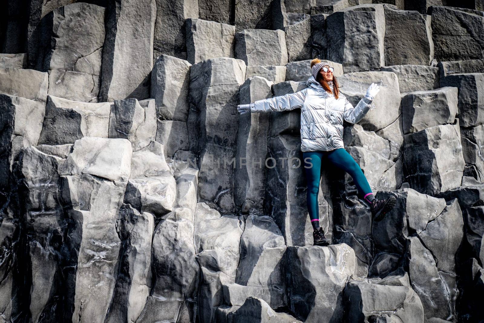 Woman in silver coat and beanie next to basalt formations in Reynisfjara, Iceland