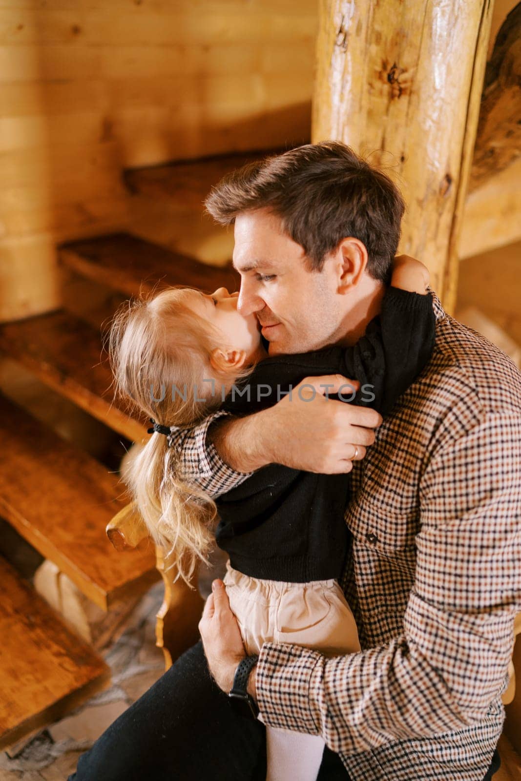 Dad hugs a little girl sitting on his lap near the stairs, looking away. High quality photo