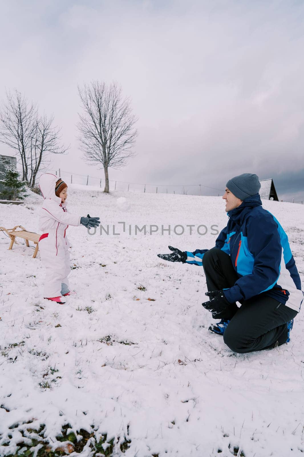 Little girl throws a snowball into the hands of her father, who is squatting, while standing on a snowy hill. High quality photo