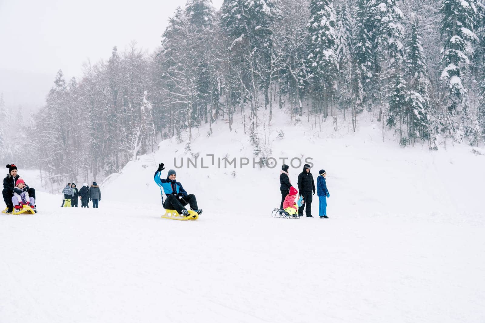 Adults and children sledding down a snowy mountain by Nadtochiy