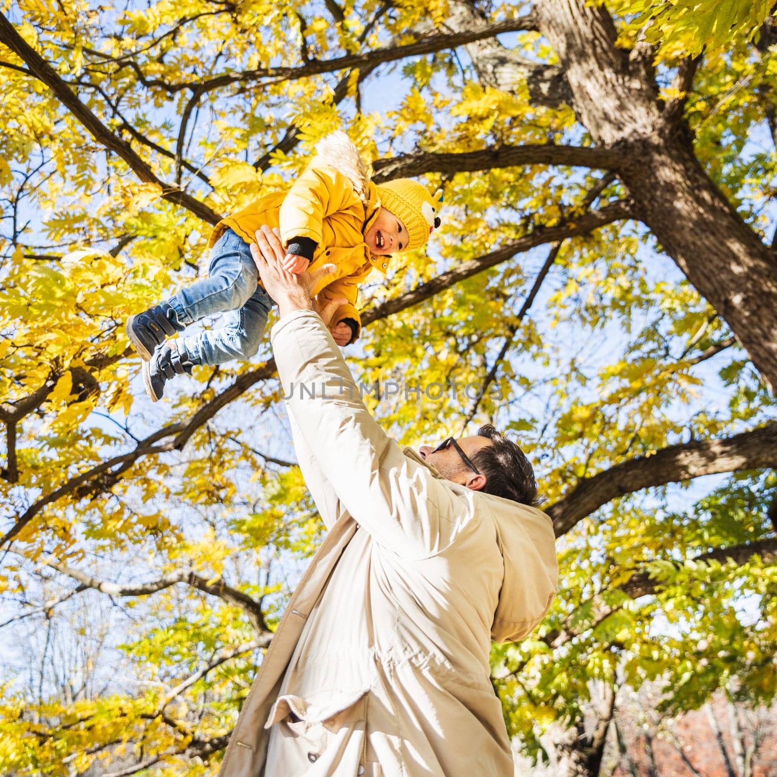 More, more,...dad, that's fun. Happy young father throws his cute little happy baby boy up in the air. Father's Day, Father and his son baby boy playing and hugging outdoors in nature in fall. by kasto