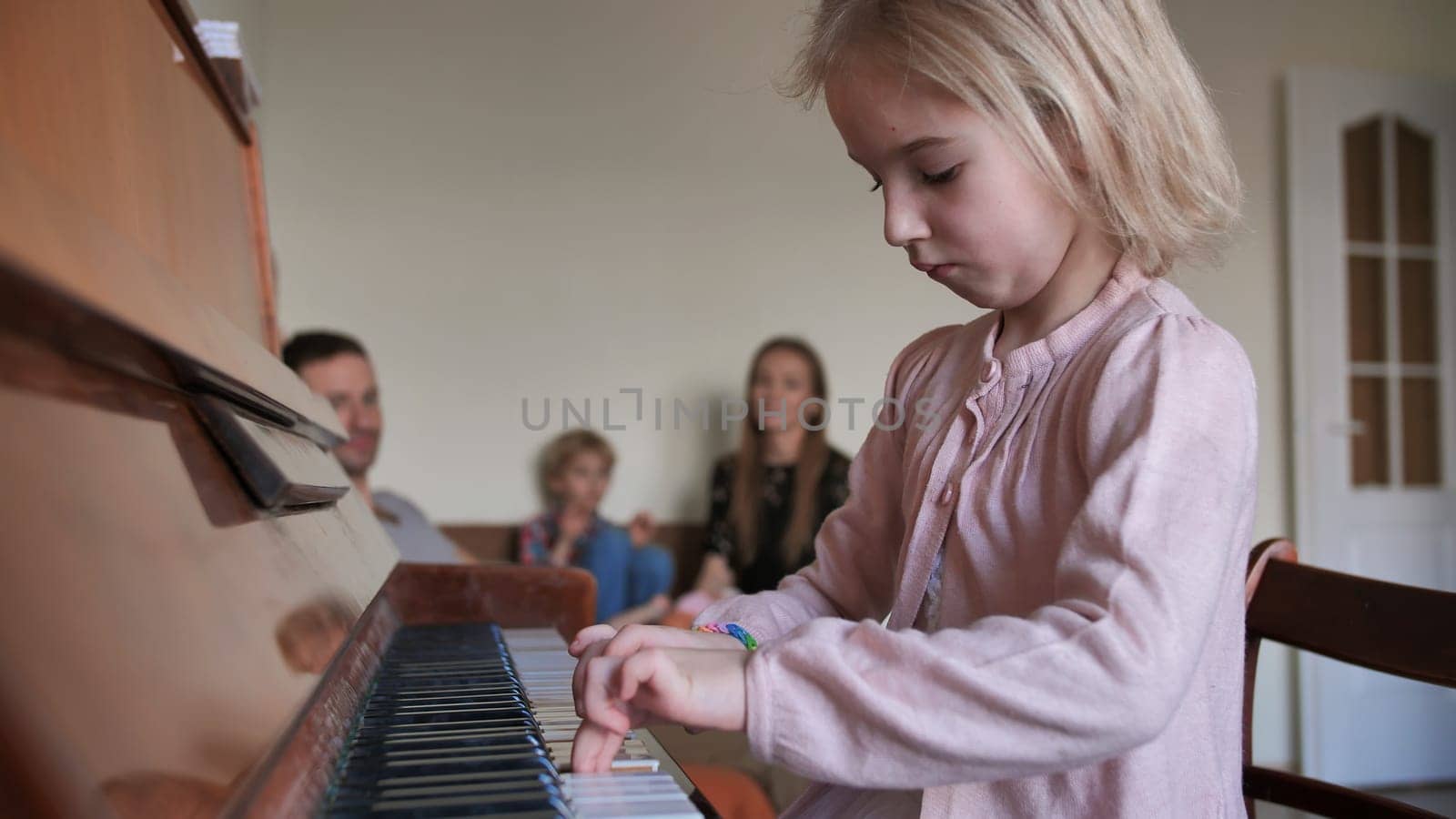 A six-year-old girl plays the piano with her family and her parents applaud her