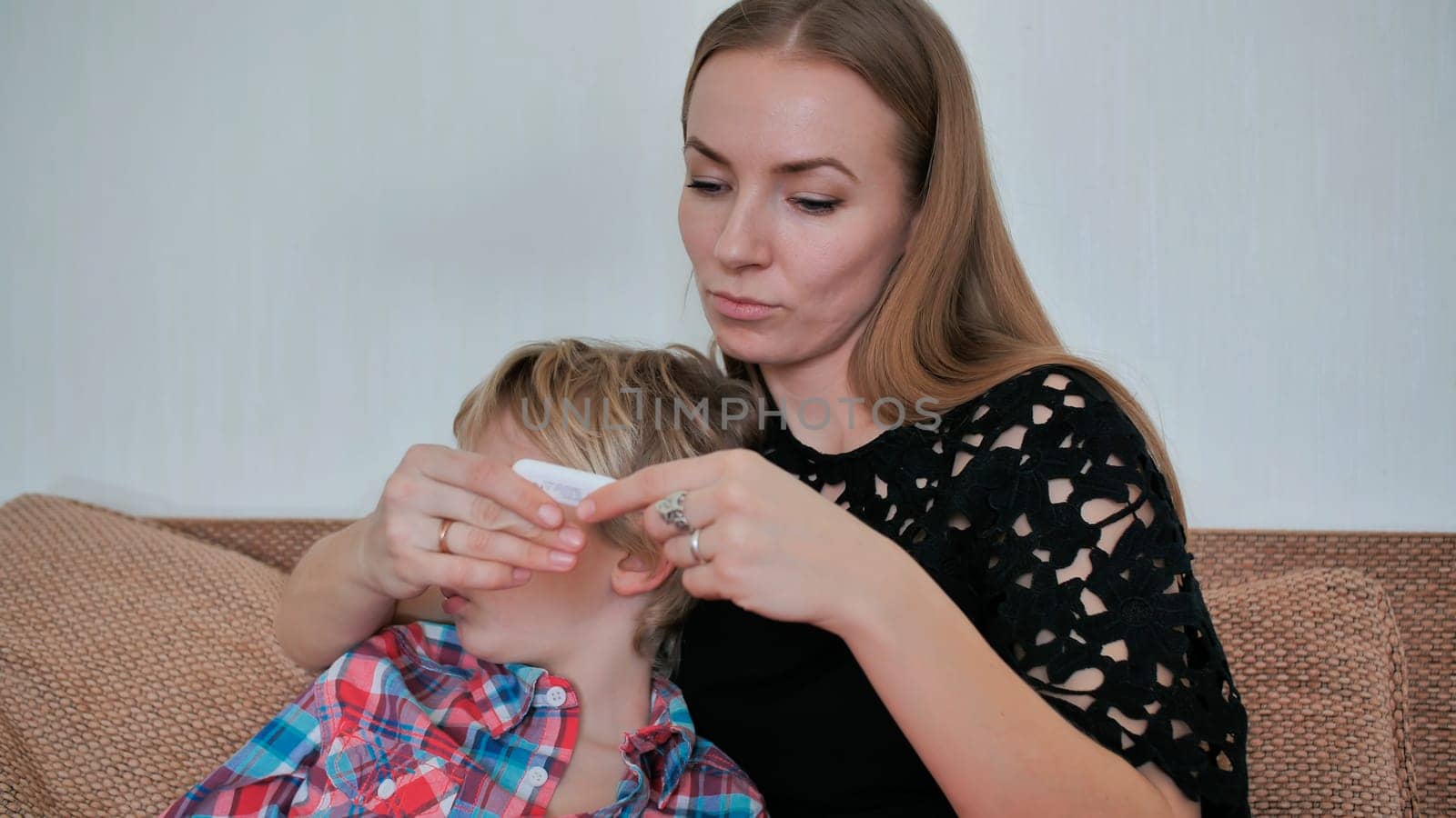 A caring mother measures the temperature of her son with a thermometer