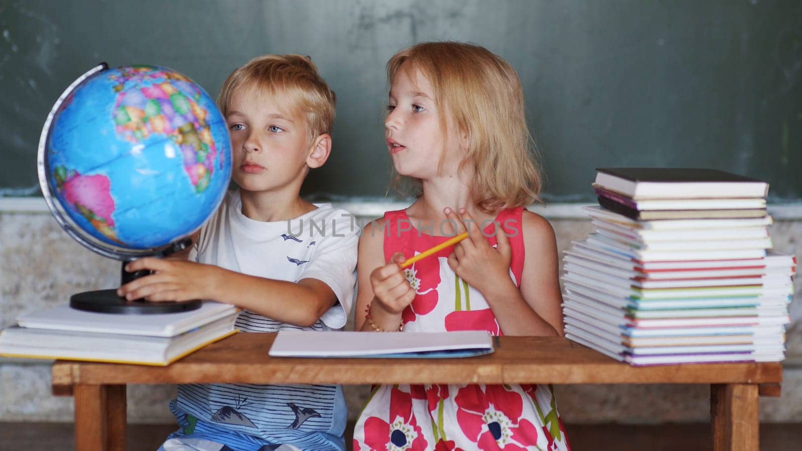 Brother and sister study at home with a world globe. by DovidPro