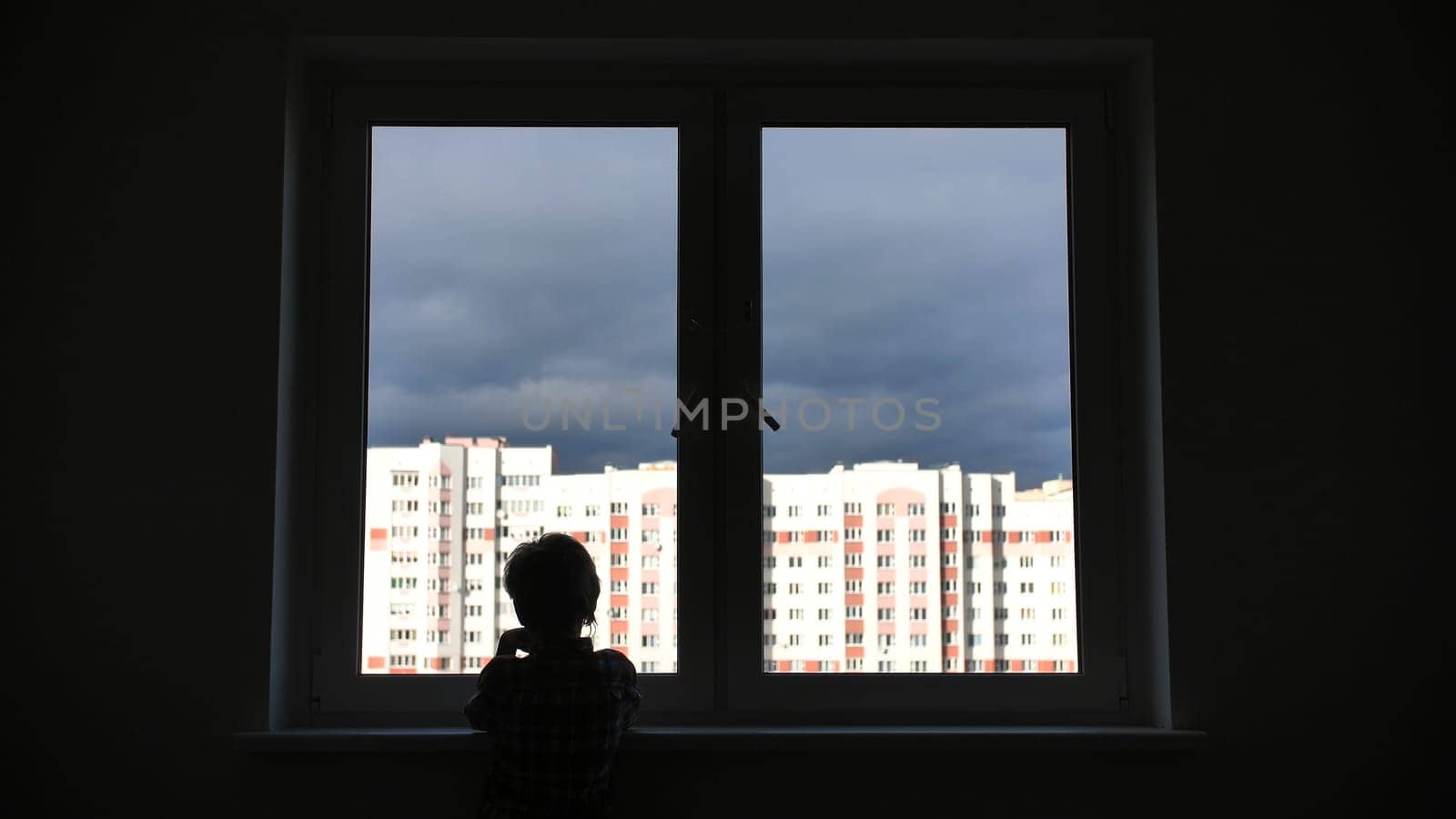 A lonely child looks out the window of his house in an apartment
