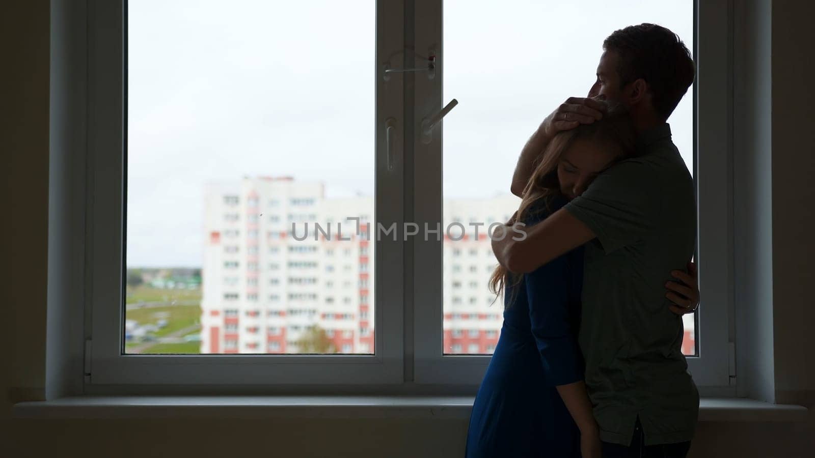 Silhouette of hugging loving couple on the background of the apartment window. by DovidPro