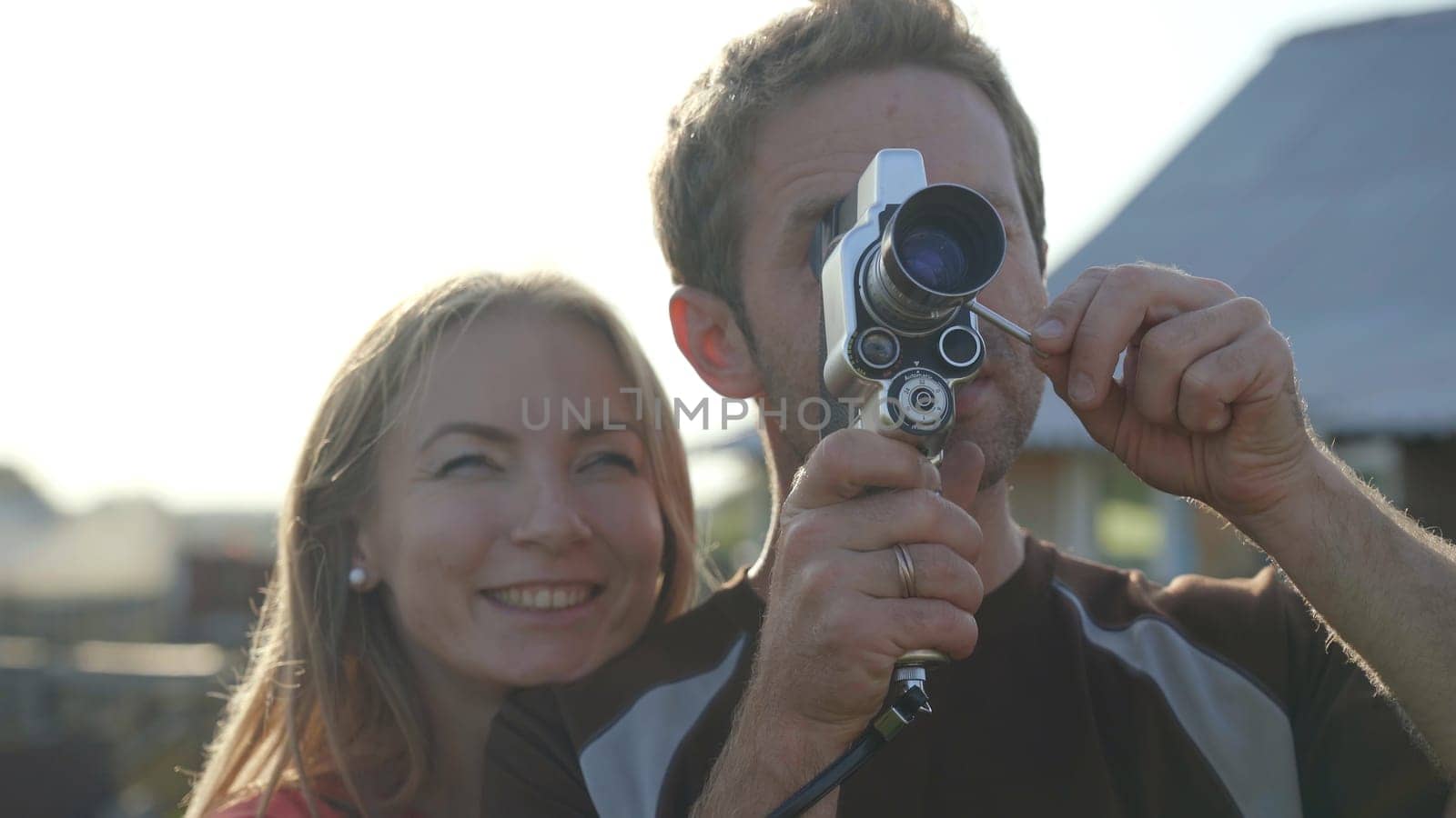 A young guy next to his girlfriend is filming a video on a retro video camera from the 60s. by DovidPro