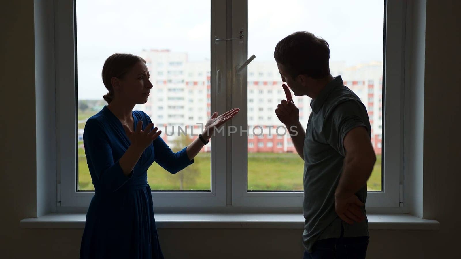 Silhouette of young spouses swearing on the background of the window of their apartment