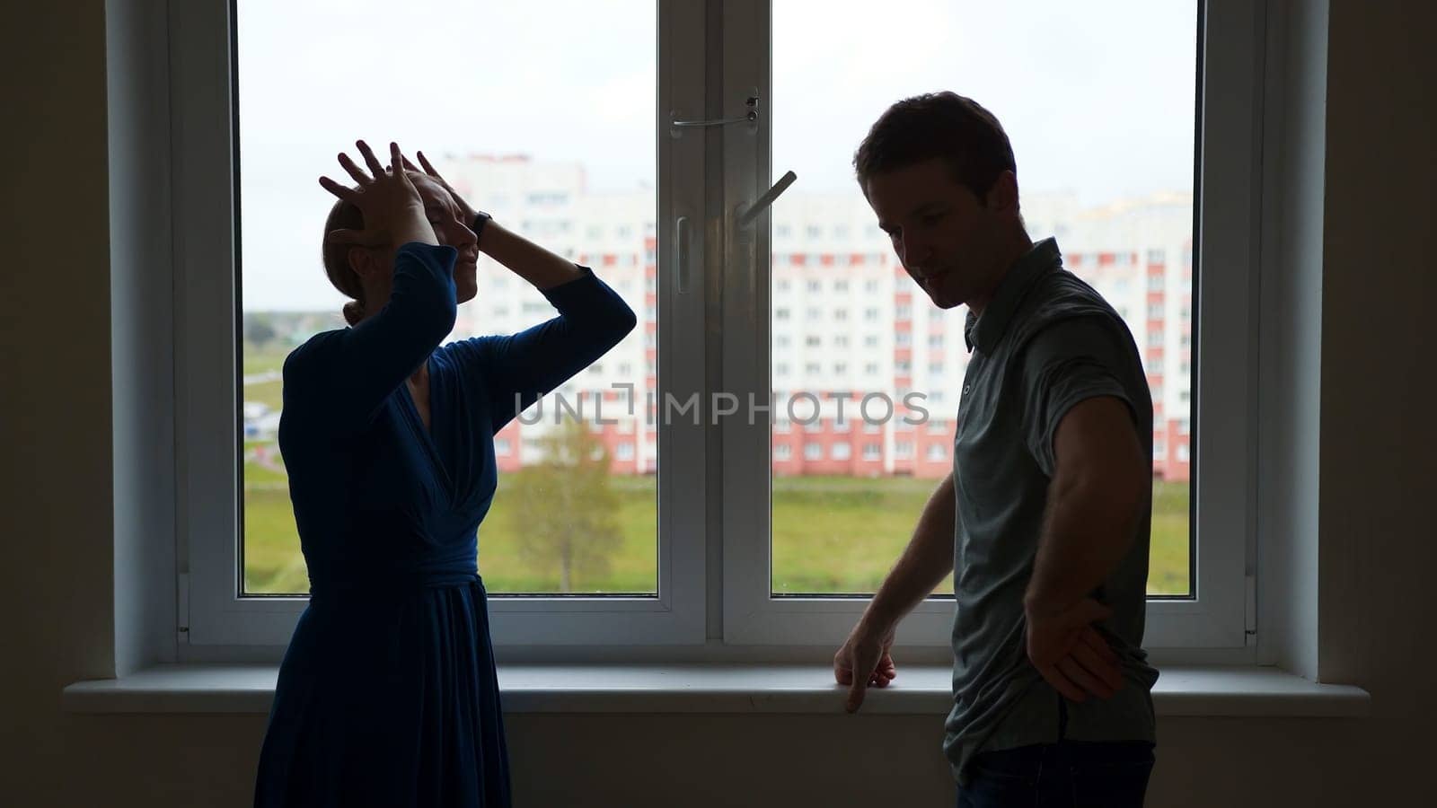 Quarantine concept. Silhouette of young spouses swearing on the background of the window of their apartment. by DovidPro
