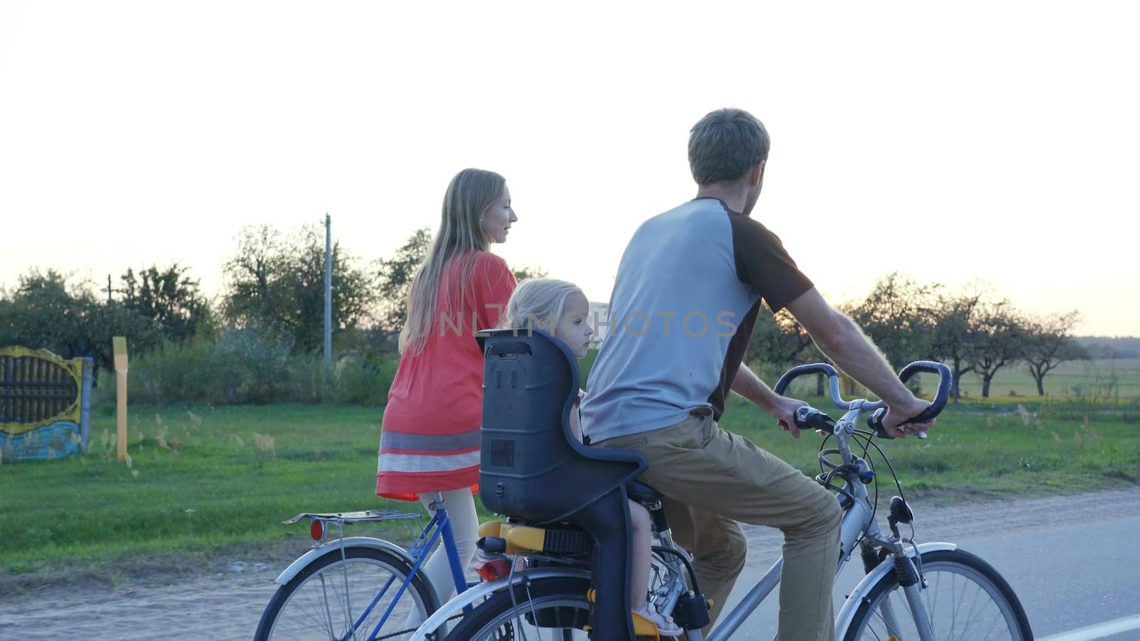 Young couple on a bike with their little daughter at sunset. by DovidPro