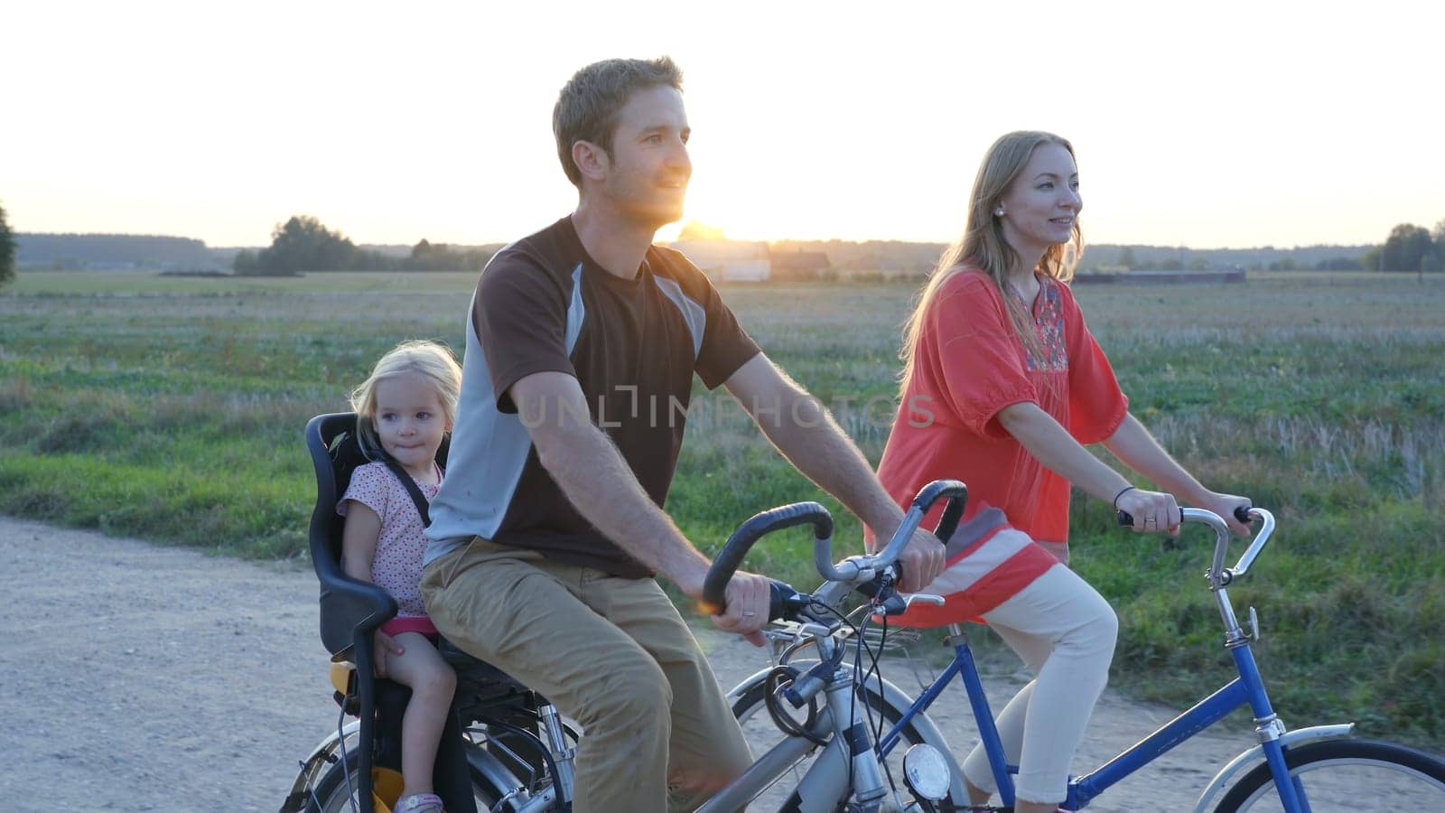 Young couple on a bike with their little daughter at sunset