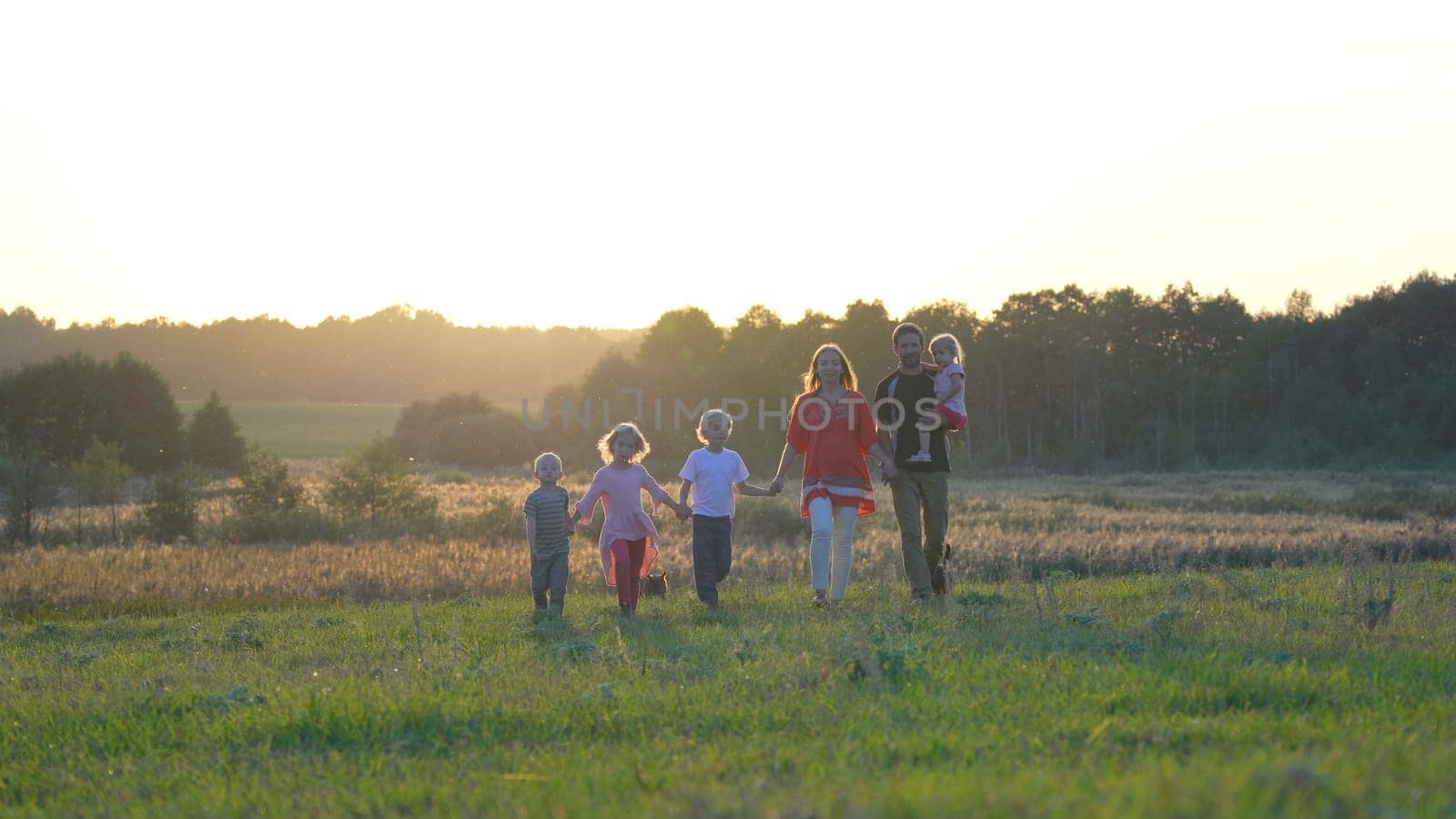 A large friendly family walks across the field at sunset