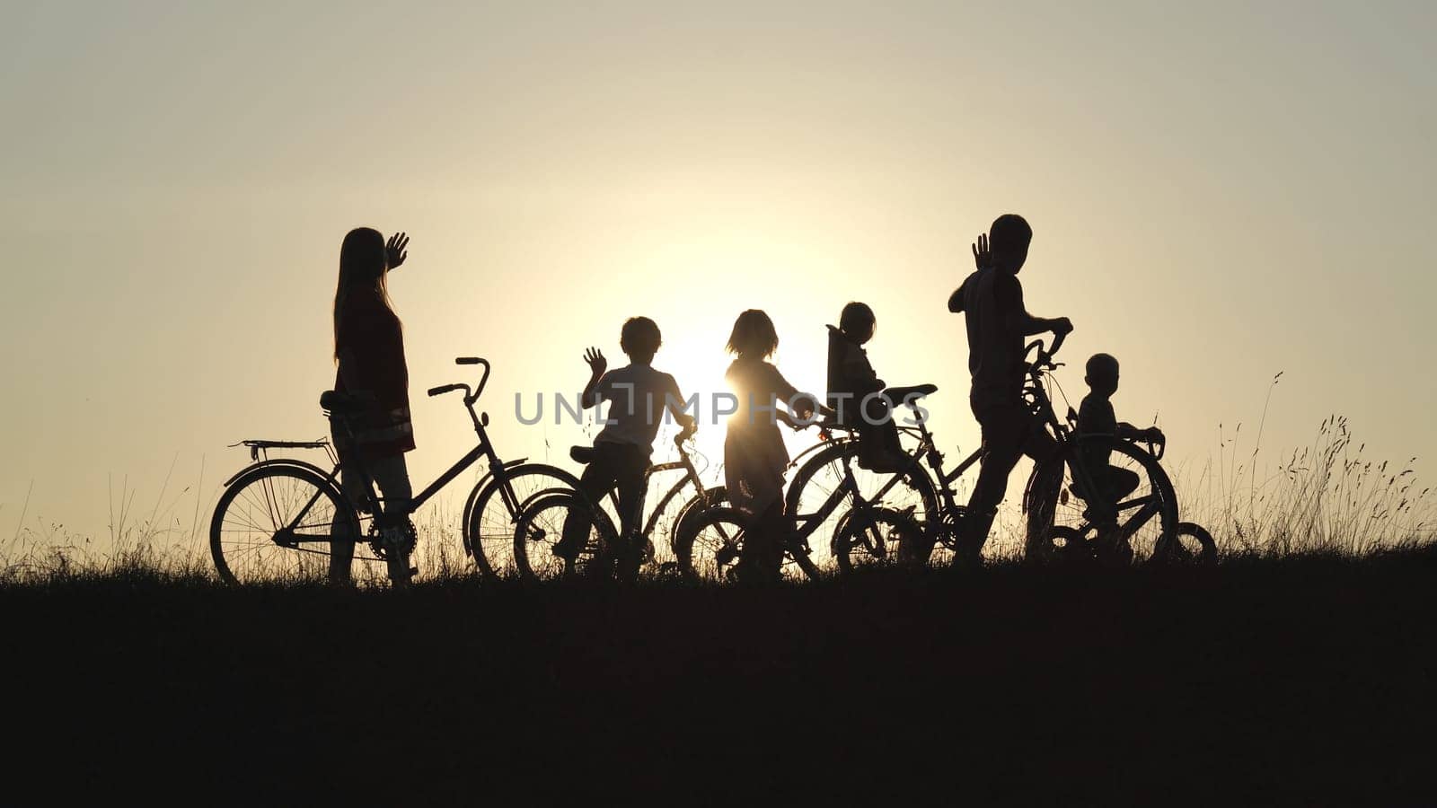 Silhouettes of a large large family waving their hands to the sun with bicycles and dogs at sunset. by DovidPro