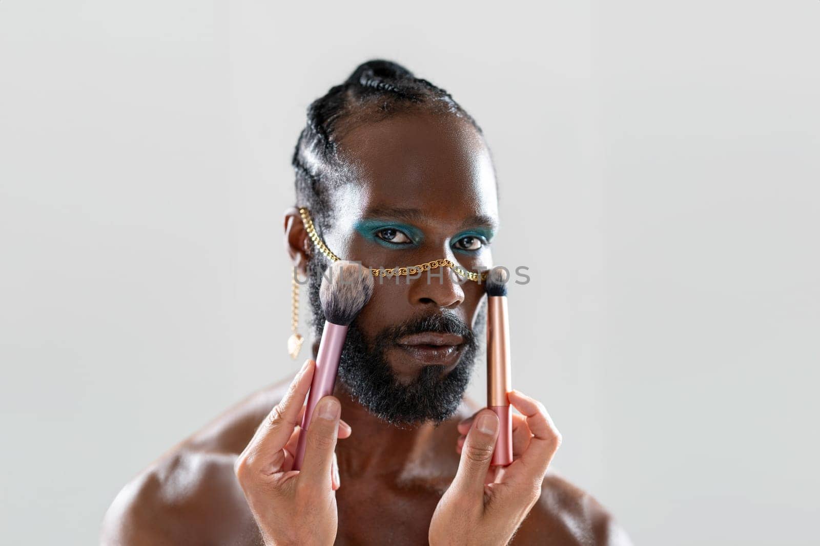 African gay applying make up holding makeup brush in hand. Close up portrait homosexual man looking at camera ready for apply visage on face. Fashion lgbt concept.