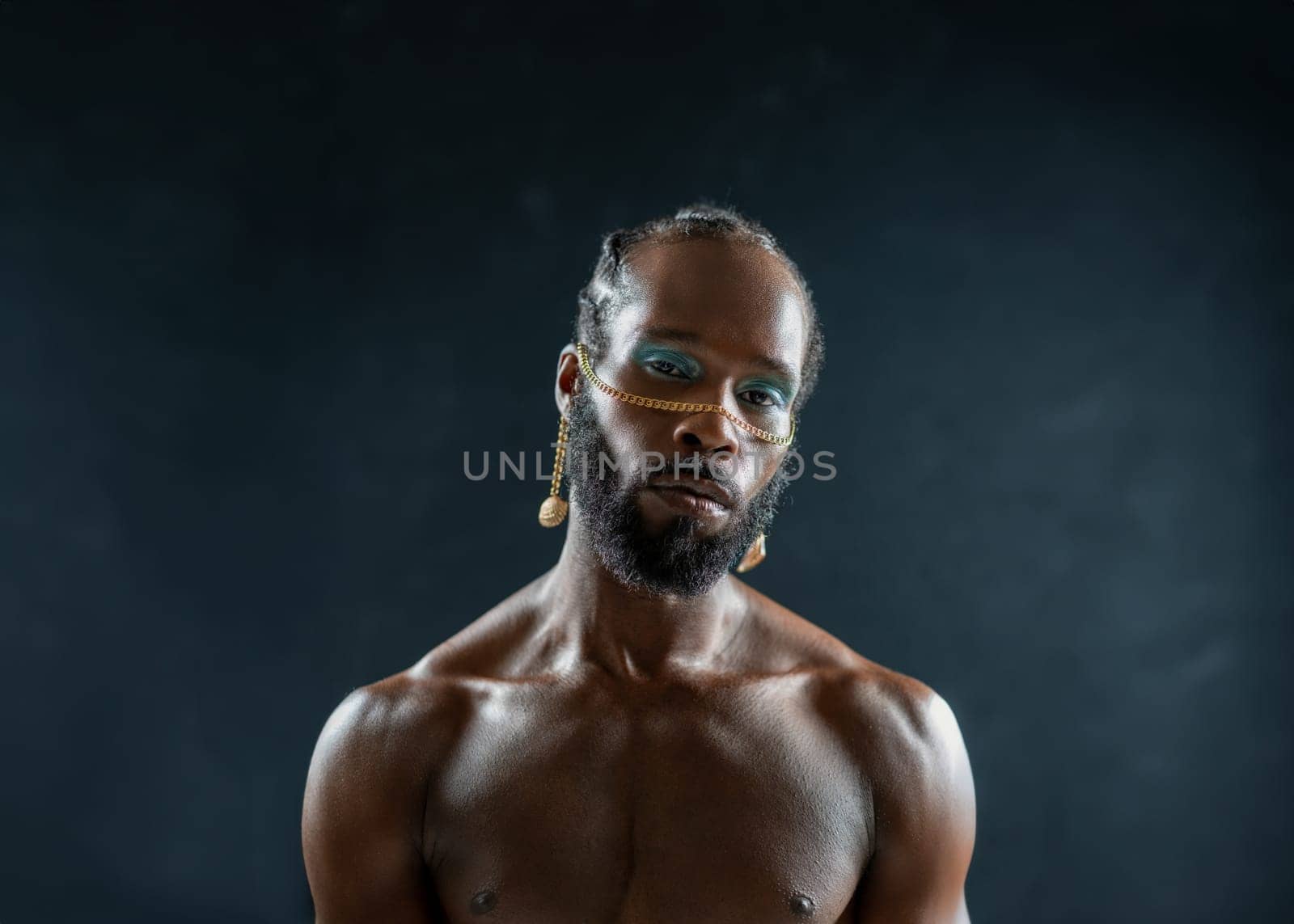 Confident african-american bearded gay man with bright makeup isolated on black, Close up portrait gay African muscular shirtless man wearing make-up looking at camera.