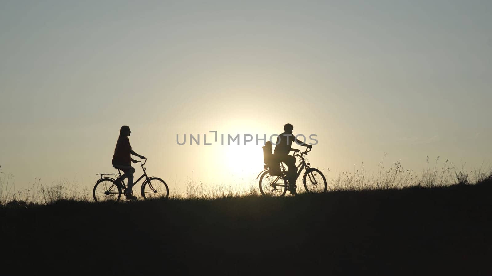 Friendly family with a child on bicycles during sunset. by DovidPro