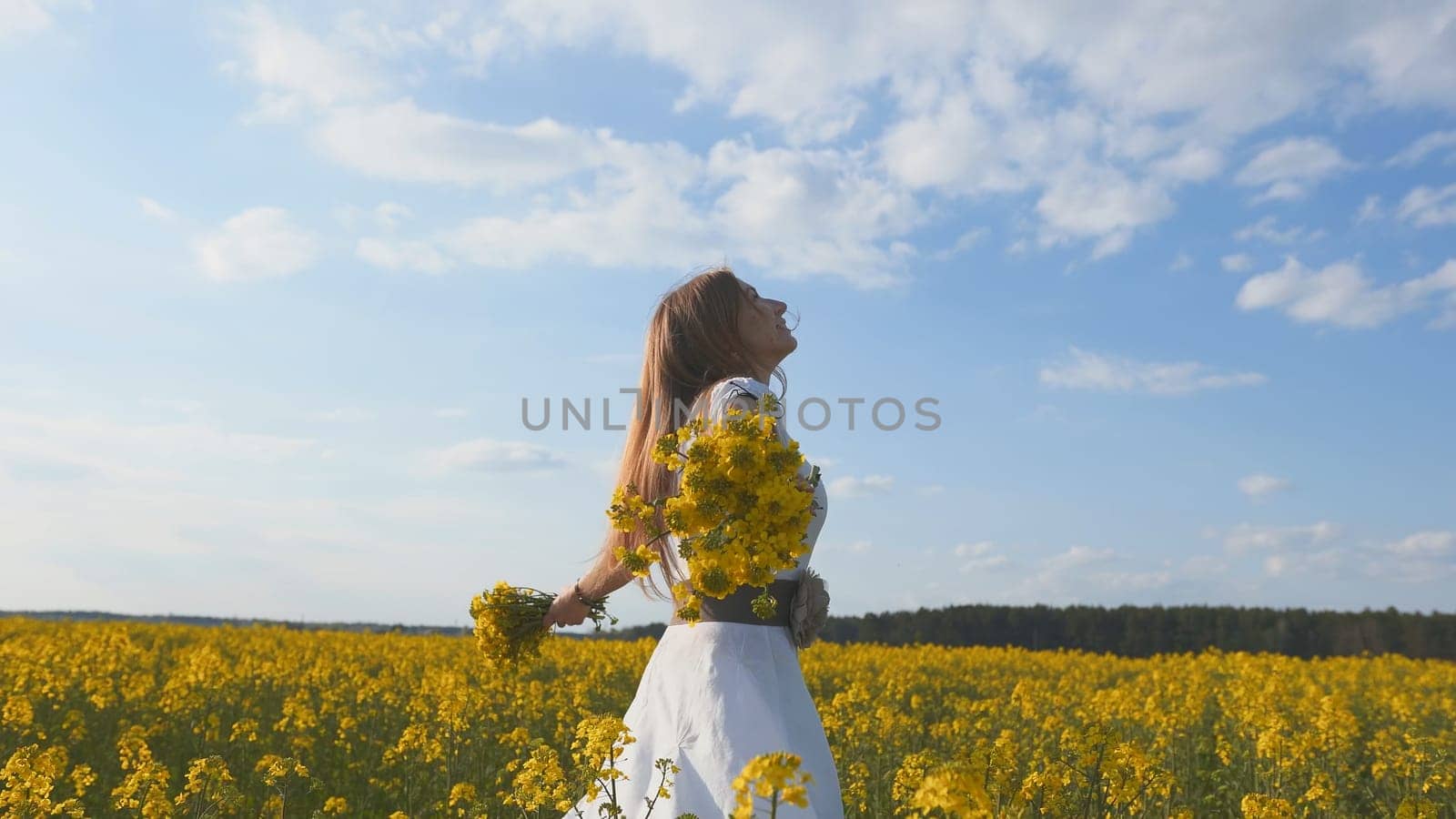 A girl in a white dress is spinning among a rapeseed field