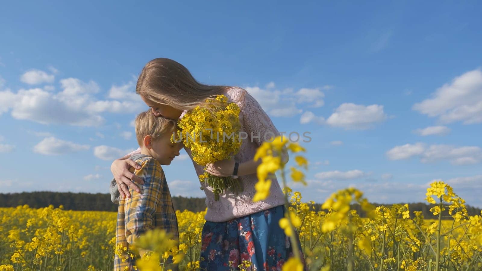 A loving son gives his mother rapeseed flowers in a rapeseed field