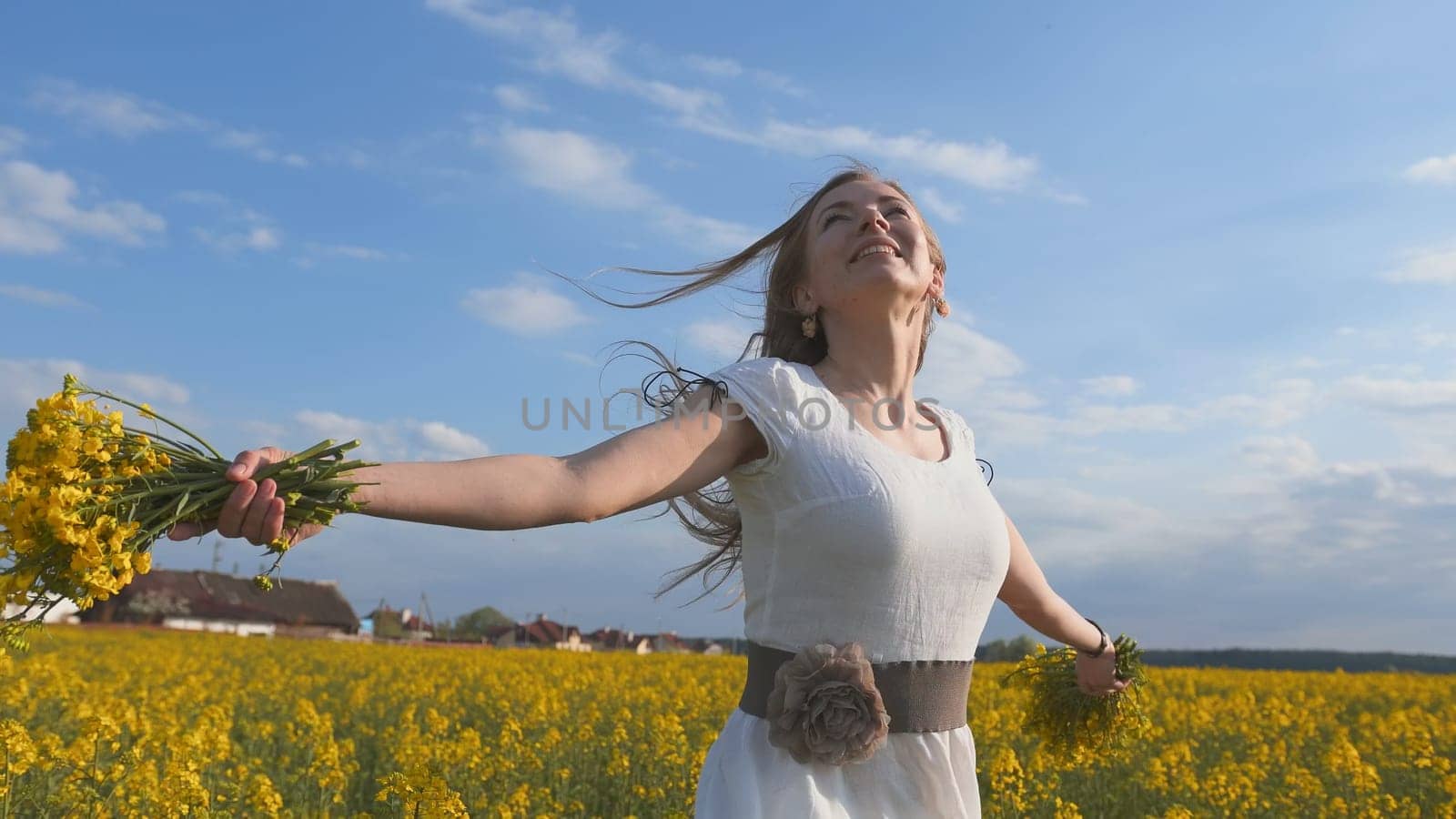 Happy girl in a white dress with a bouquet of rapeseed flowers in a yellow rapeseed field