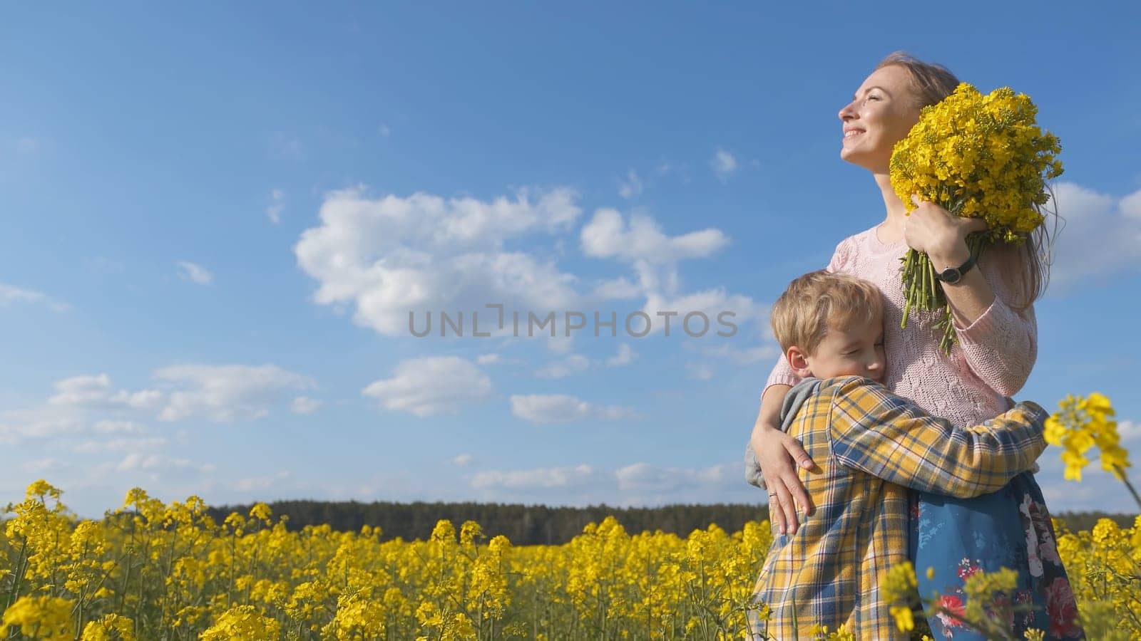 A loving son hugs his mother in a rapeseed field. by DovidPro