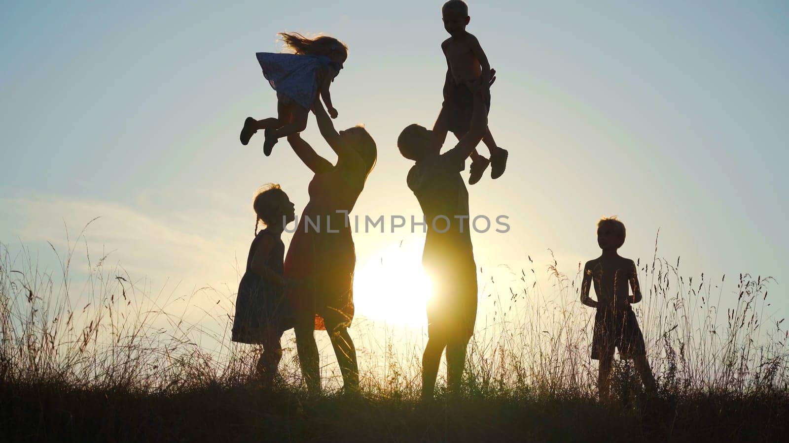 Happy parents toss their children up against the sunset