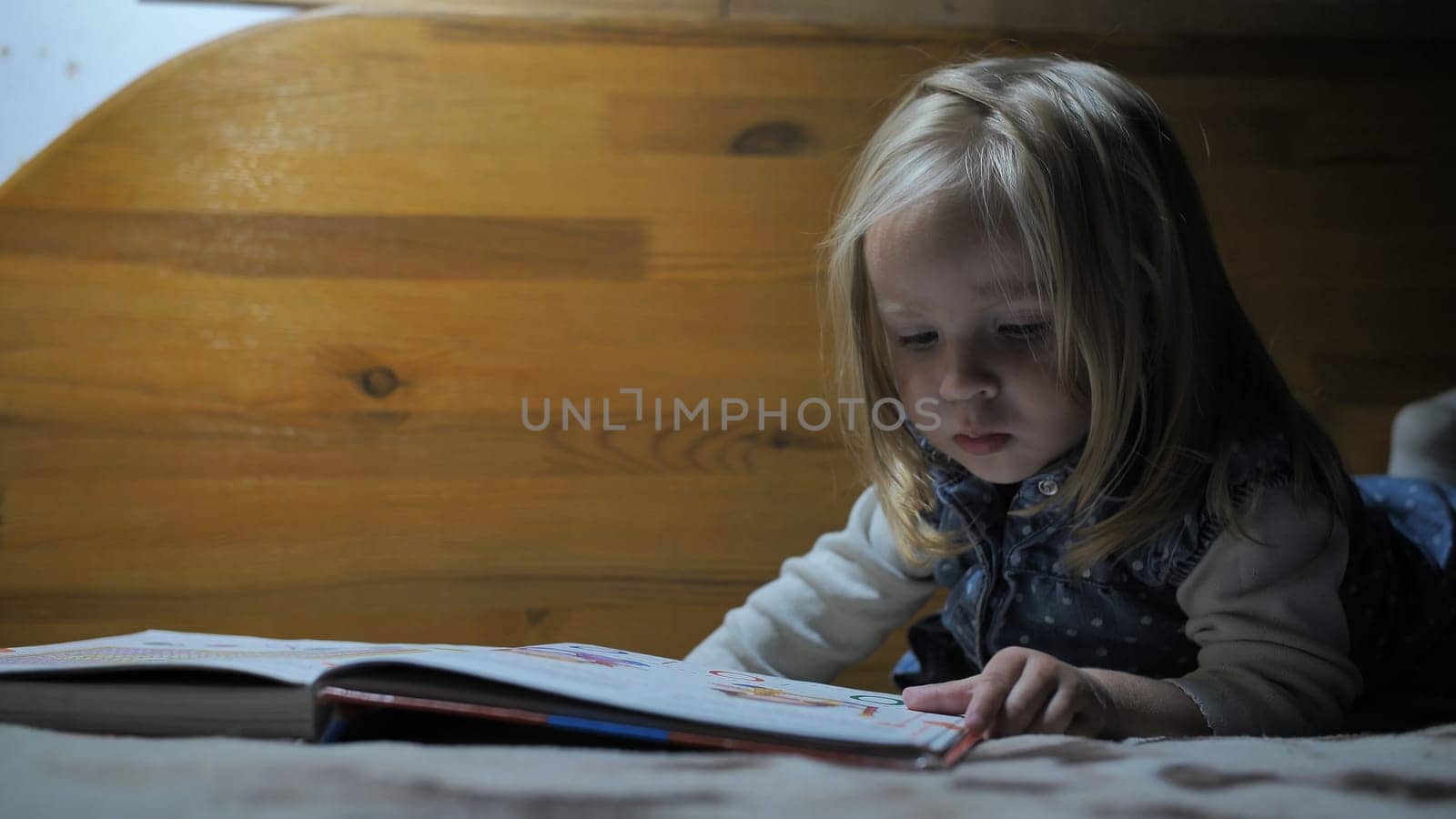 Little girl leafing through pages of a book by the light of a lamp