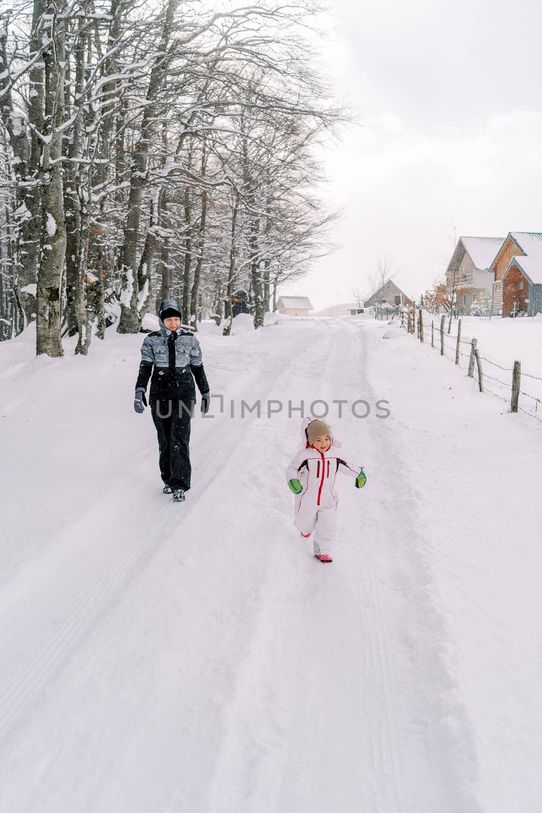 Mother and a little girl walk along a snowy road in a village at the edge of the forest. High quality photo