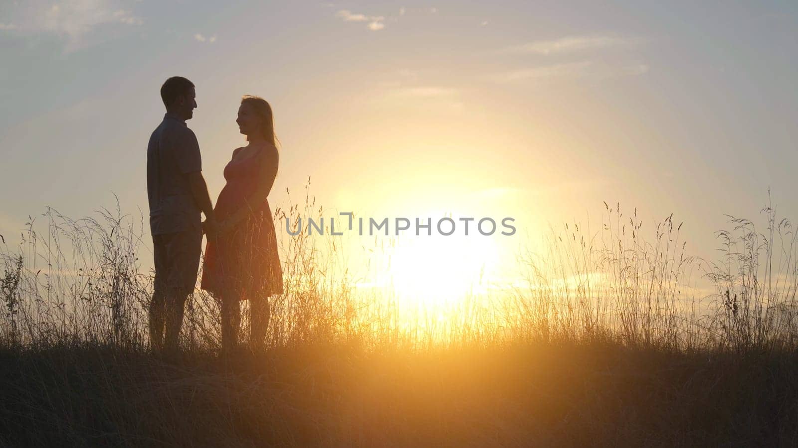 Silhouettes of happy young parents against the background of the evening sun