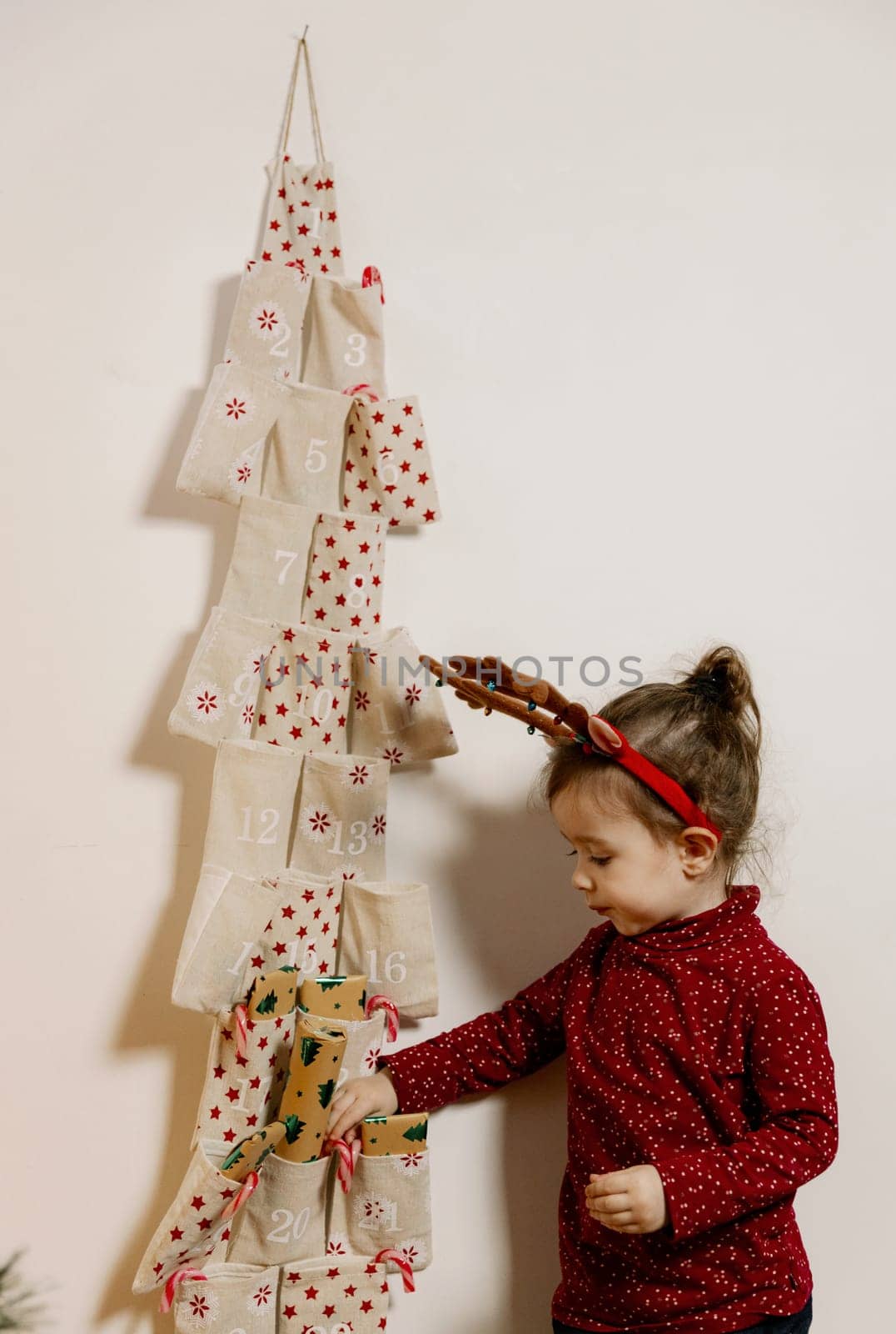 One little Caucasian girl takes out a gift from the pocket of a wall advent calendar with her hand, close-up side view.