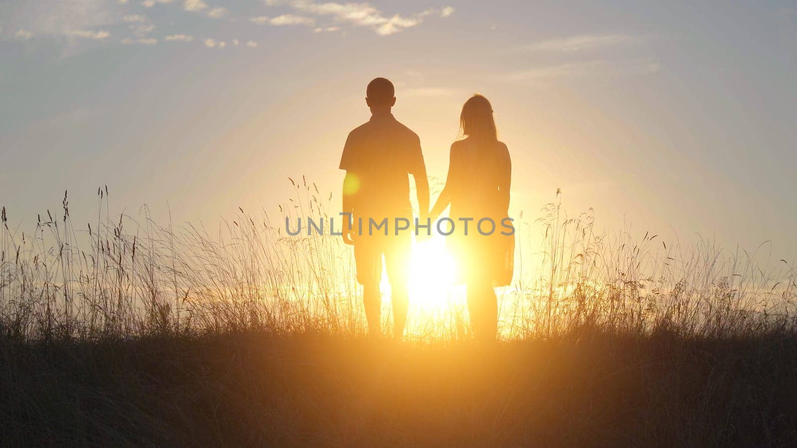 Happy lovers silhouettes stand against the background of the evening sun. by DovidPro