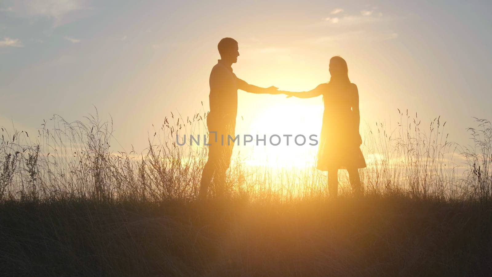 A beautiful young couple at sunset stretch their hands to each other