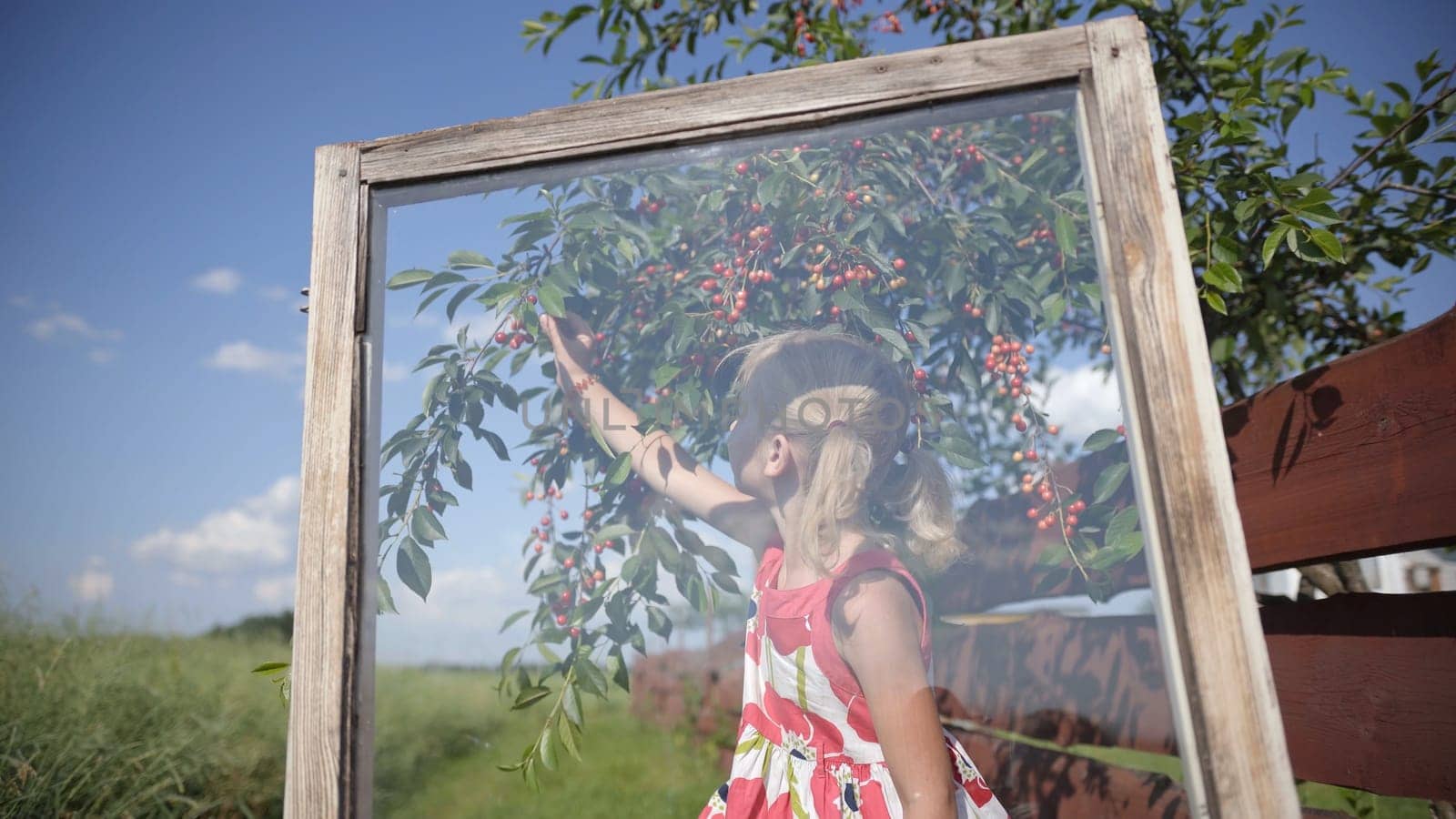 A little girl eats cherries on the background of a window in the garden