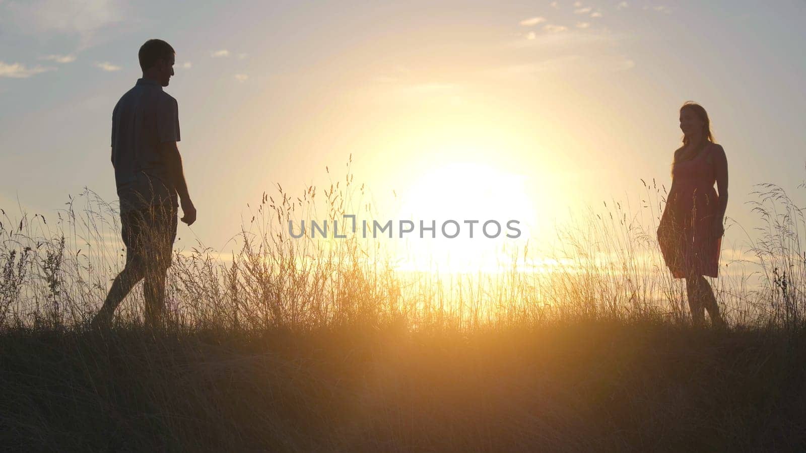 Silhouettes of young parents meeting on the background of the beautiful evening sun and parting right there. by DovidPro