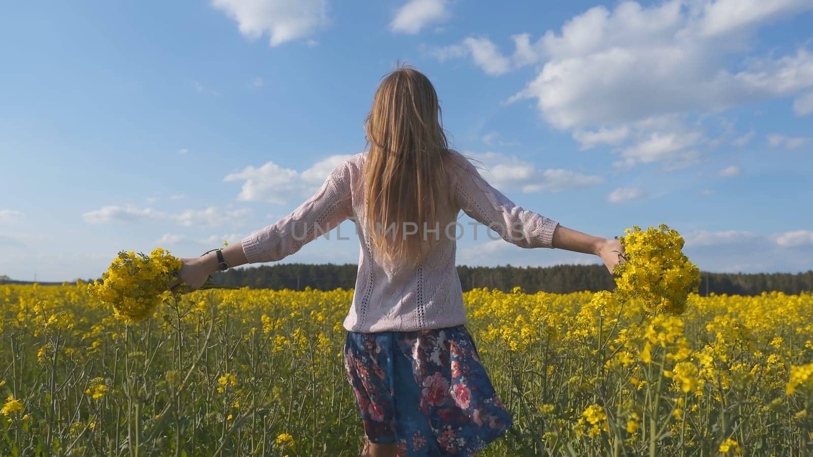 A girl in a white dress is walking among a rapeseed field