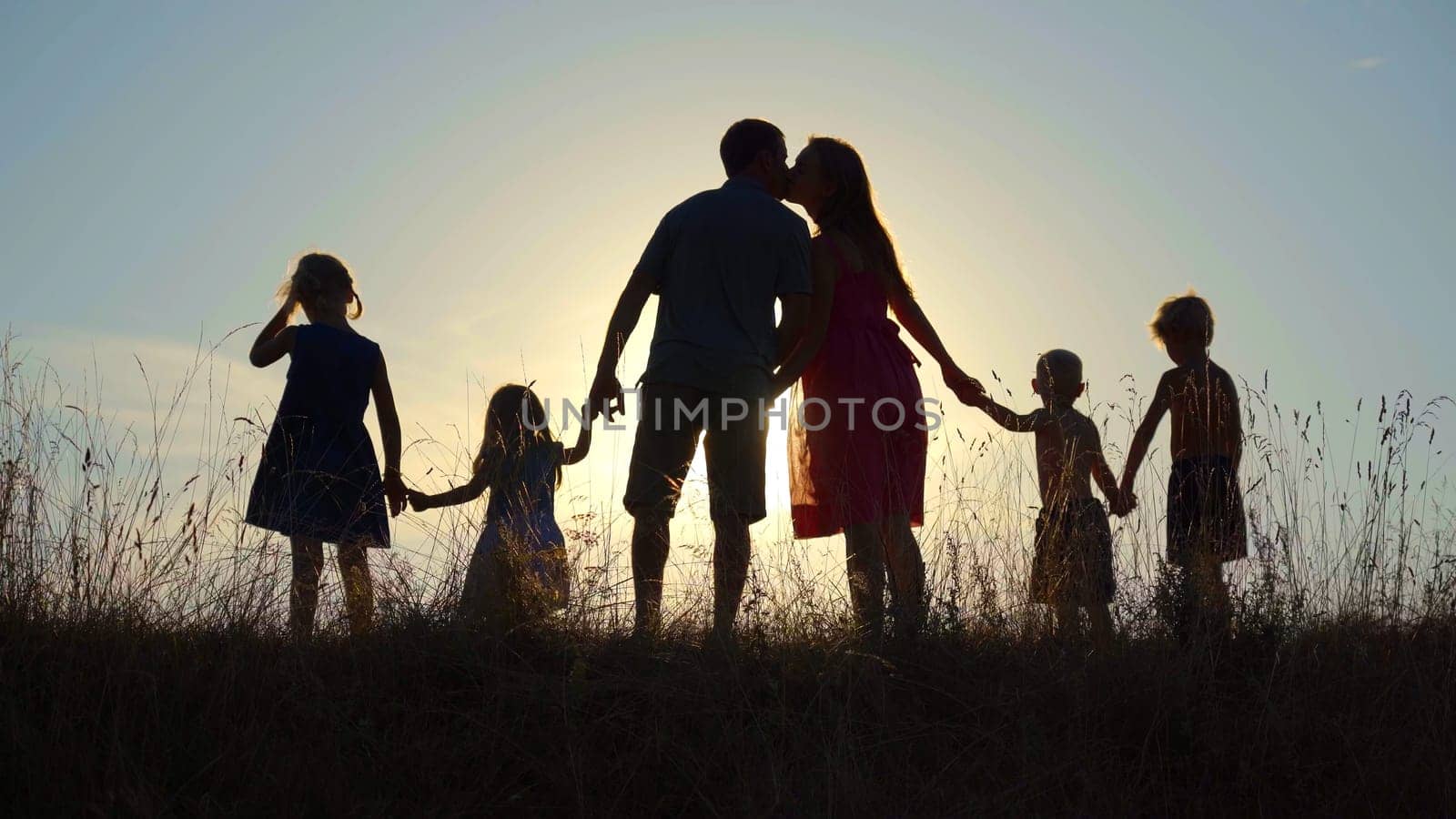 Happy parents kiss at sunset while holding the hand of their children. by DovidPro