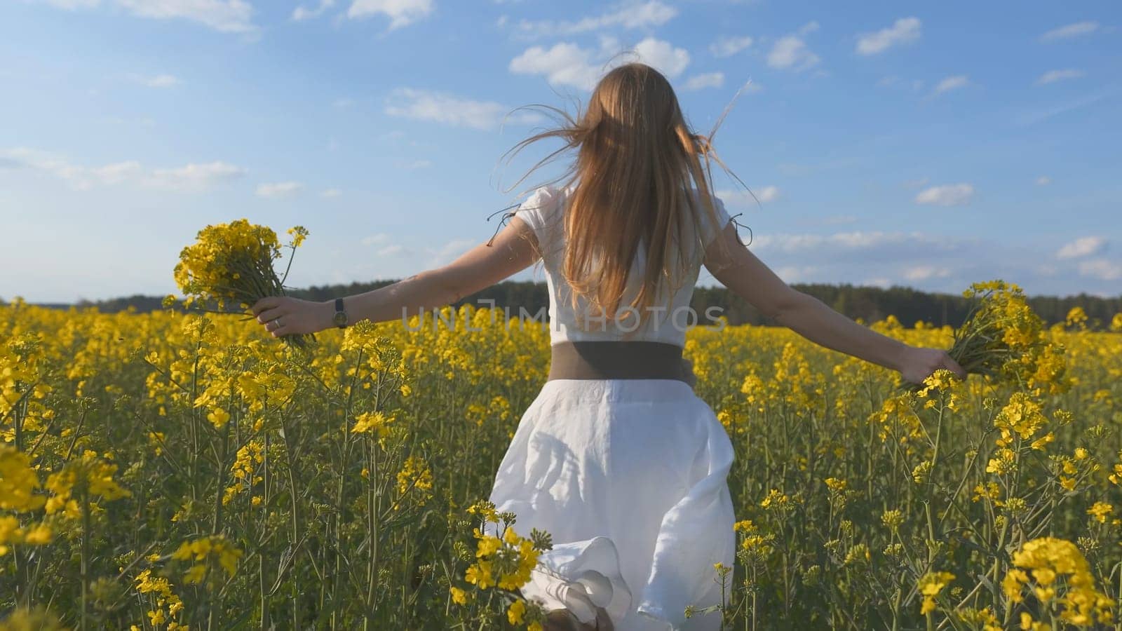 A girl in a white dress runs among a rapeseed field