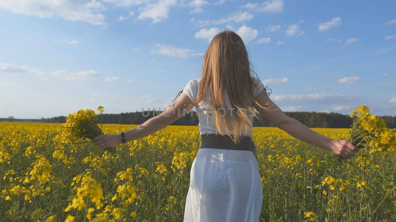A girl in a white dress runs among a rapeseed field