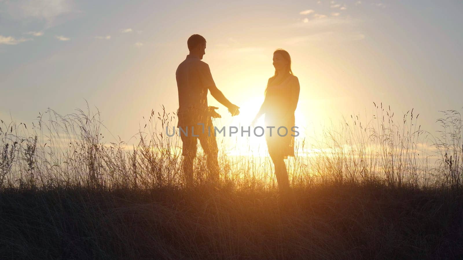 Silhouettes of young parents meeting on the background of the beautiful evening sun and parting right there
